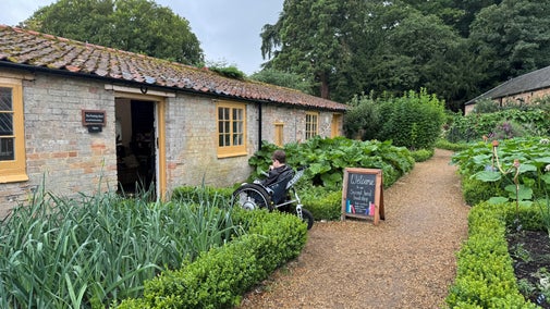 A young wheelchair user in the kitchen garden at Oxburgh, about to enter the bookshop.